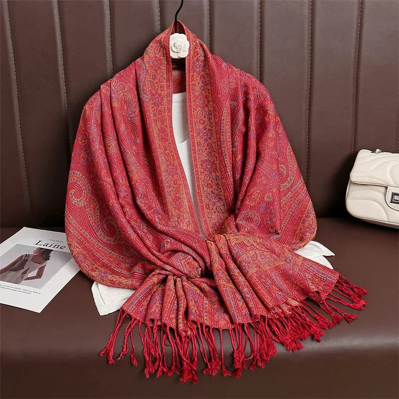 Red paisley pashmina scarf with tassels displayed on brown sofa beside a white purse
