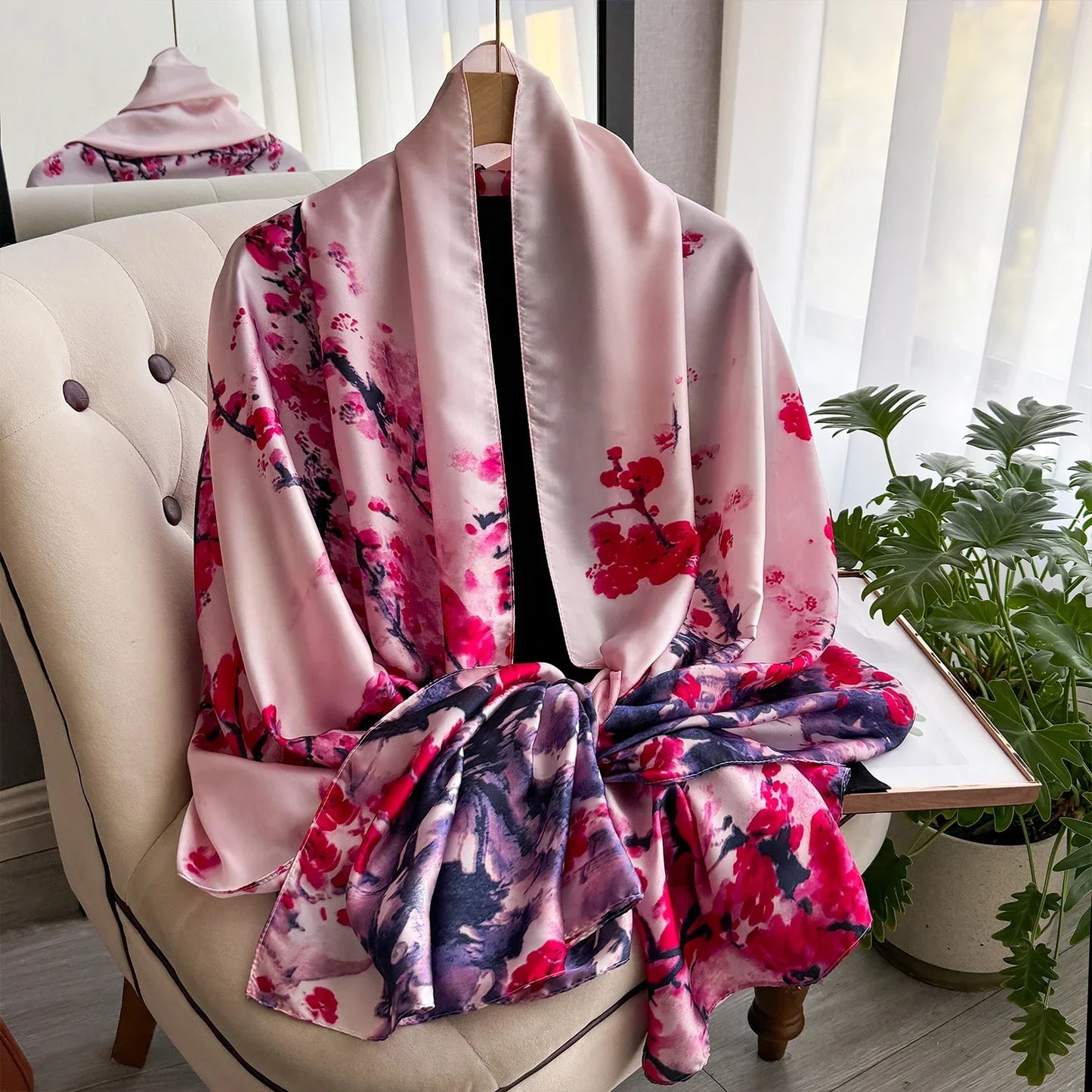 Pink floral silk kimono draped on a chair by a window with sheer curtains and a plant