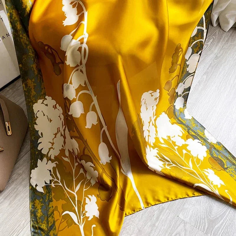 Yellow silk scarf with white floral print and green border on wooden floor