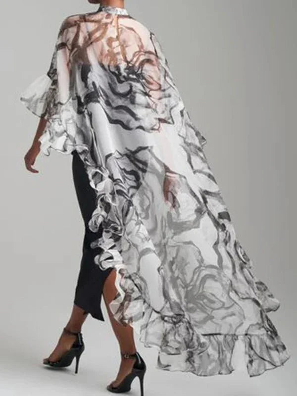 Woman wearing sheer black and white ruffled cape over black dress and heels, fashion style