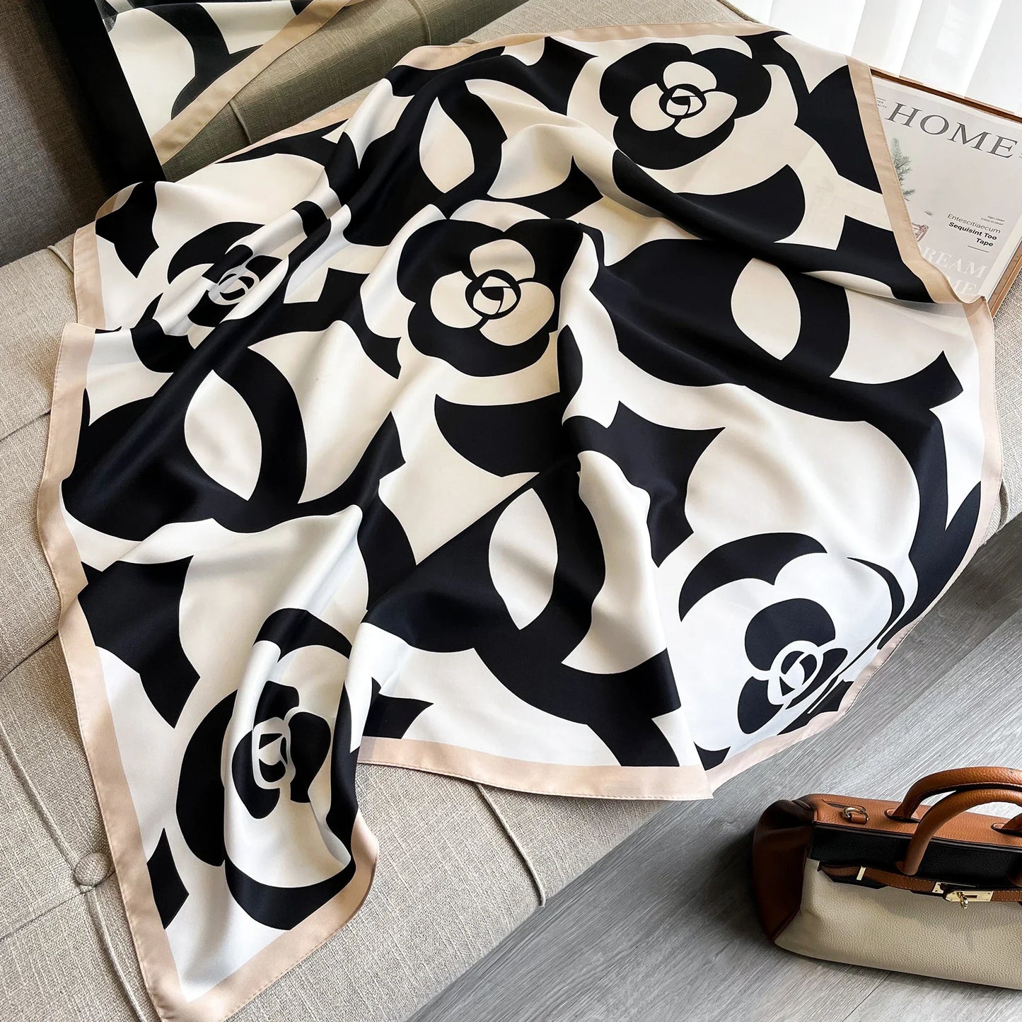 Black and white floral silk scarf with beige trim on sofa, next to tan and cream handbag