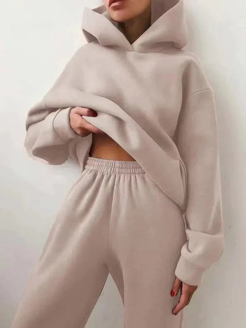Woman wearing beige oversized hoodie and sweatpants matching lounge set against white wall