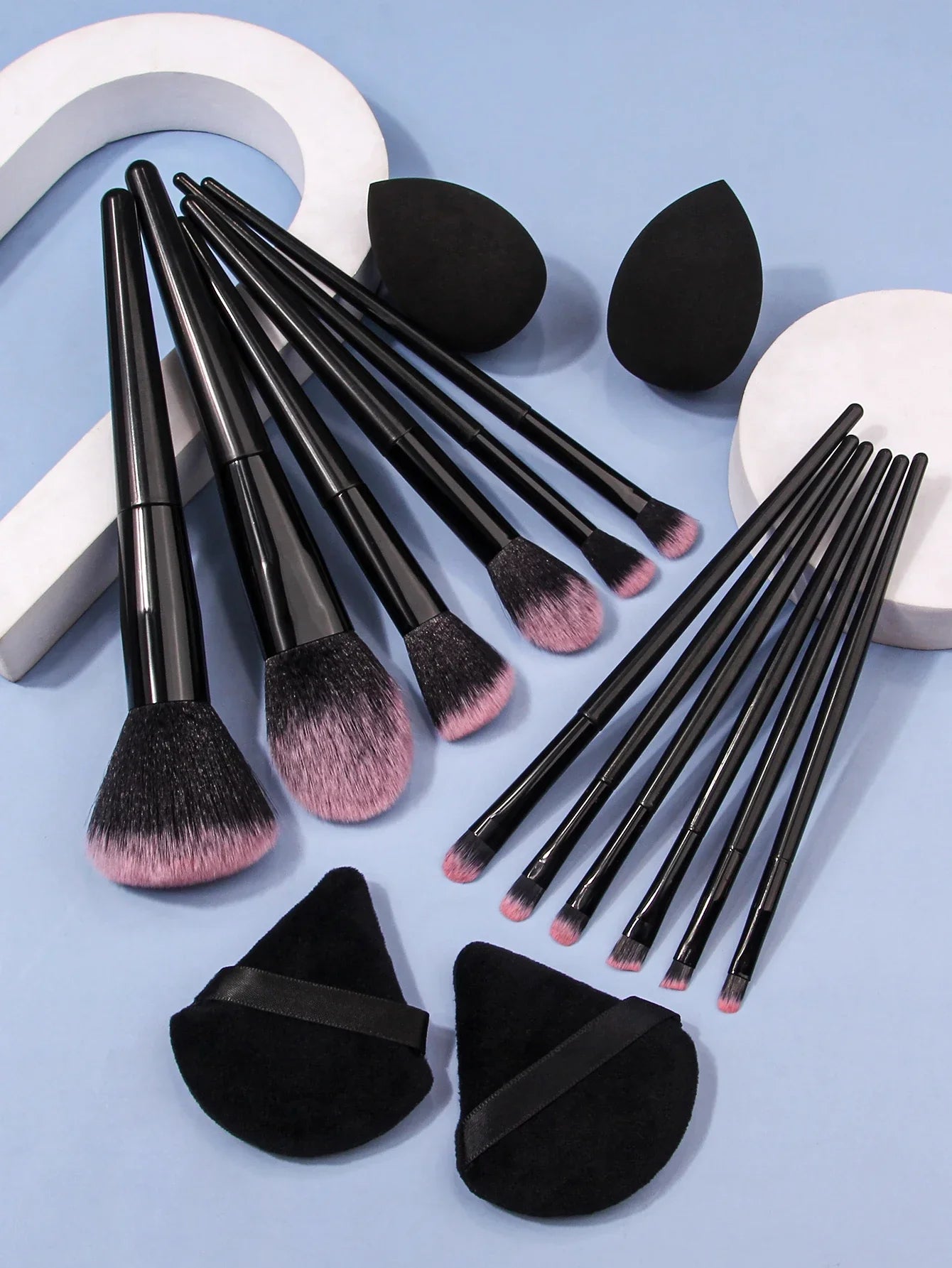 Luxury soft makeup brush set with black handles, pink bristles, sponges, and powder puffs on blue background