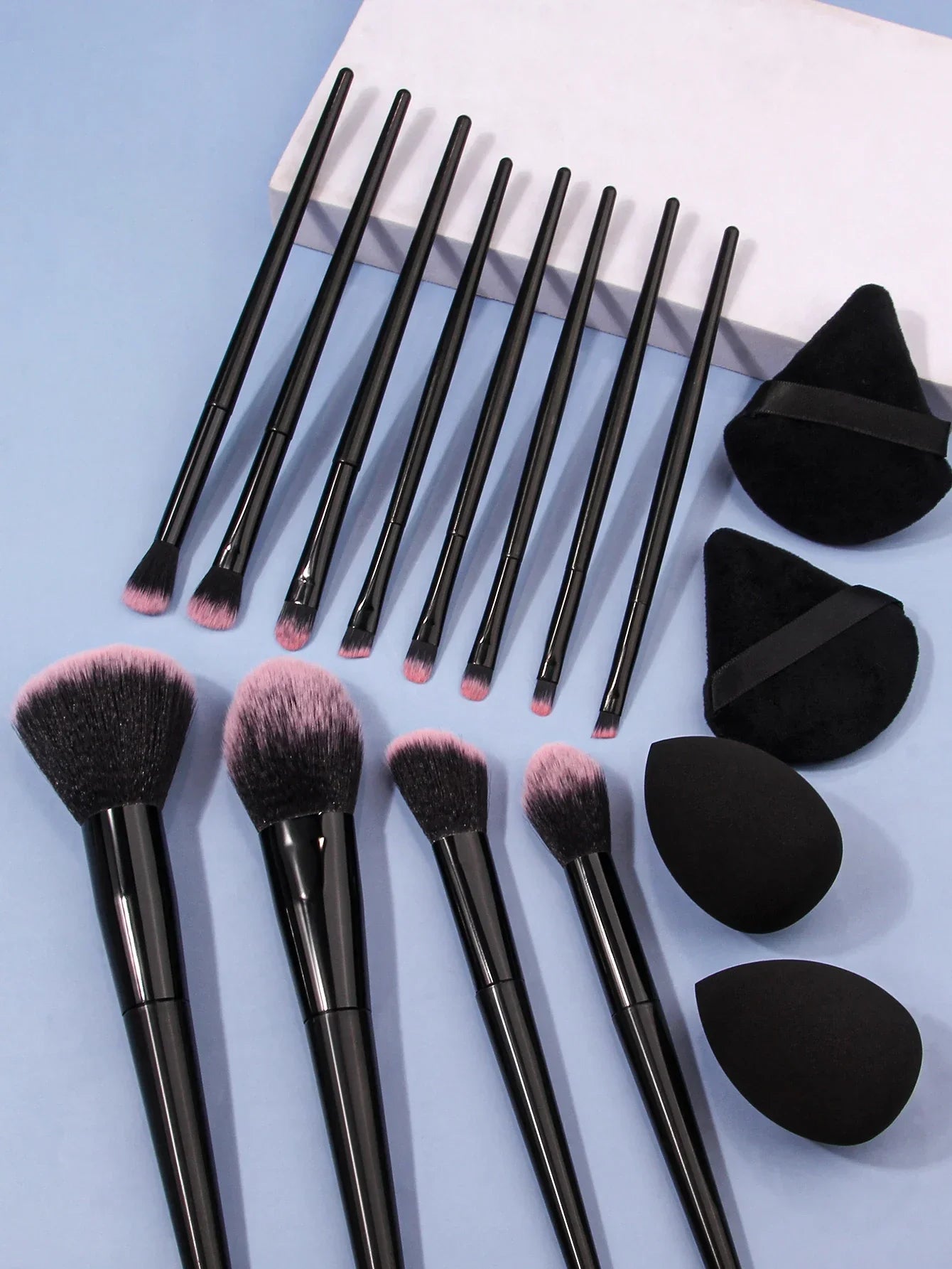 Luxury soft makeup brush set with black handles and blending sponges on blue background