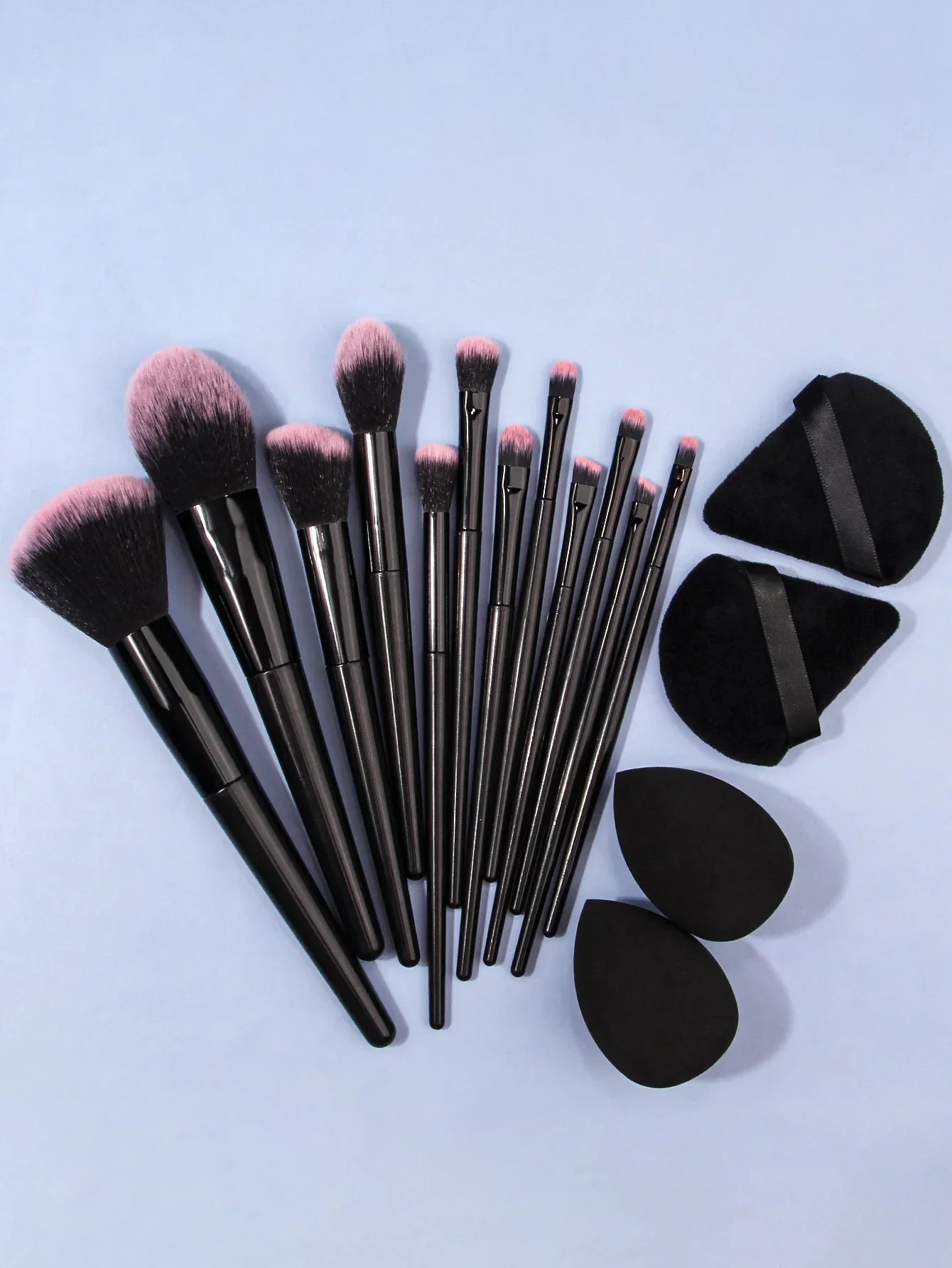 Luxury black makeup brush set with pink tips, sponges, and powder puffs on light blue background