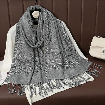 Gray paisley patterned scarf with fringe displayed on white sweater and brown sofa