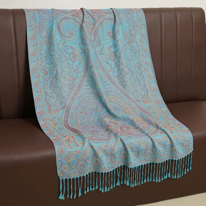 Light blue paisley patterned throw blanket with fringe draped over a brown sofa