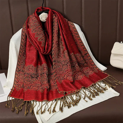 Red paisley pashmina scarf with gold tasseled fringe draped on a white top and brown seat