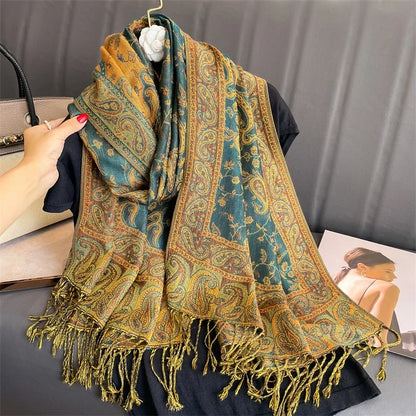 Paisley pattern green and gold scarf with fringe, displayed on a black top, hand holding edge