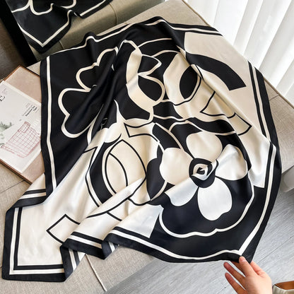 Black and white floral silk scarf with bold graphic pattern on a beige sofa