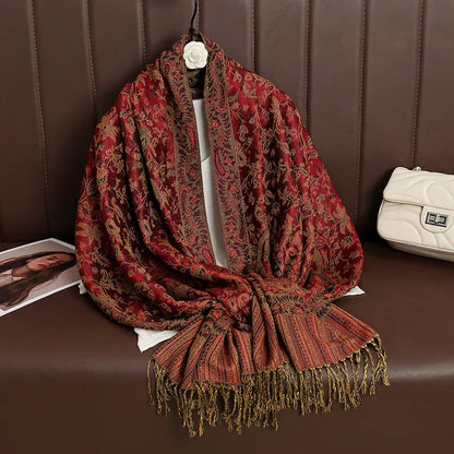 Red paisley jacquard shawl with gold fringe on a brown sofa, next to white purse