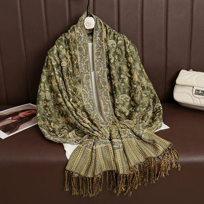 Green gold paisley embroidered shawl with fringes displayed on brown bench next to white purse