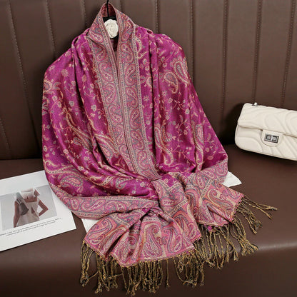 Pink paisley pashmina scarf with gold fringe on brown sofa, white quilted purse beside
