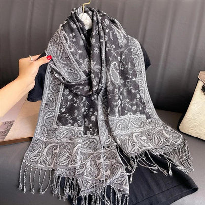 Black and gray paisley print scarf with fringed ends draped on a hanger