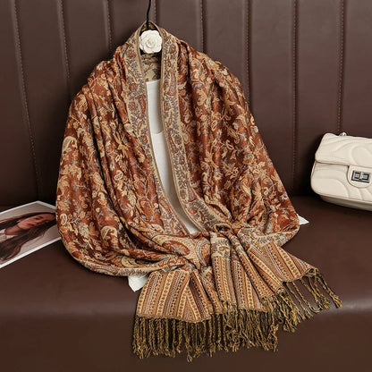 Brown paisley pashmina shawl with tasseled ends draped on a brown sofa beside a white handbag