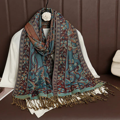 Floral patterned teal and brown fringe scarf draped over a white sweater on brown seating
