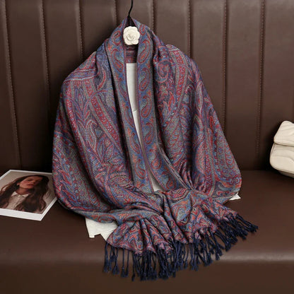 Paisley print pashmina scarf with fringe draped on brown bench, magazine and white bag nearby
