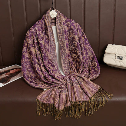 Purple gold jacquard floral shawl with fringes on brown sofa next to white quilted purse