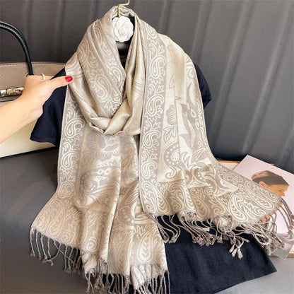 Beige paisley patterned scarf with fringes draped over a black top on a hanger