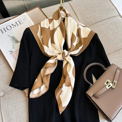 Brown and cream geometric silk scarf on black dress with taupe handbag on beige sofa