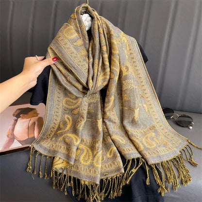 Gray and gold paisley patterned scarf with fringe, displayed on a hanger with sunglasses nearby