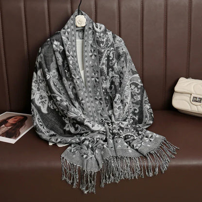 Gray paisley patterned fringed shawl draped on brown bench with beige purse