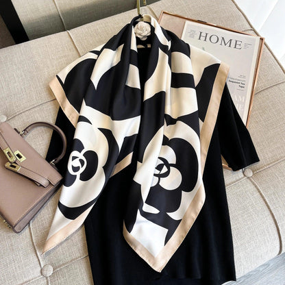 Black and white floral silk scarf on black dress, beige purse on sofa, home decor magazine nearby
