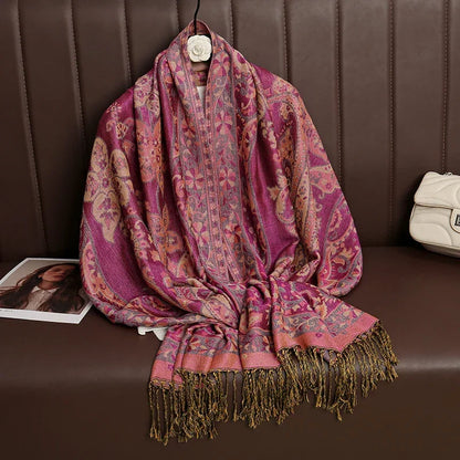 Paisley patterned pink shawl with gold fringes draped on brown seat, next to a white bag.