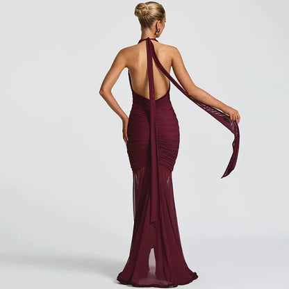 Back view of a woman wearing a long, elegant, deep burgundy halter dress with an open back and flowing fabric detail