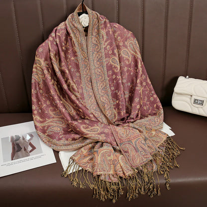 Paisley print pashmina shawl with fringe on brown leather seat, white purse nearby