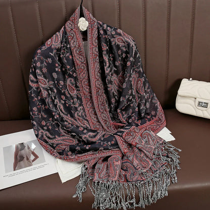 Black and red paisley shawl with fringe, displayed on brown leather seat next to white purse