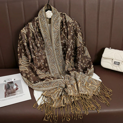 Brown paisley patterned scarf with fringe on brown leather sofa, cream handbag beside it