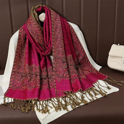 Red paisley patterned pashmina shawl with gold fringe draped on white clothing, brown seat