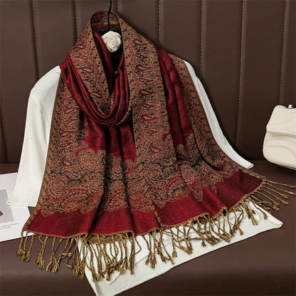 Red paisley pashmina scarf with gold fringe displayed on white fabric, luxury accessory