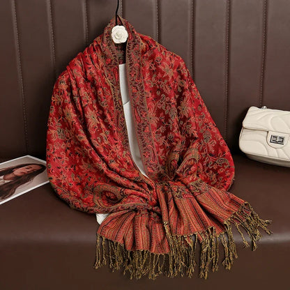 Red floral paisley shawl with fringes draped on brown leather bench next to white purse