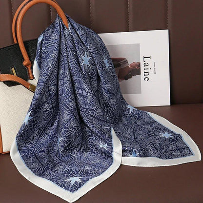 Navy blue geometric silk scarf with white border draped on a purse on a brown seat