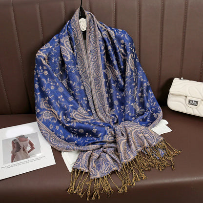 Blue paisley pashmina scarf with fringe on brown leather bench, white purse beside