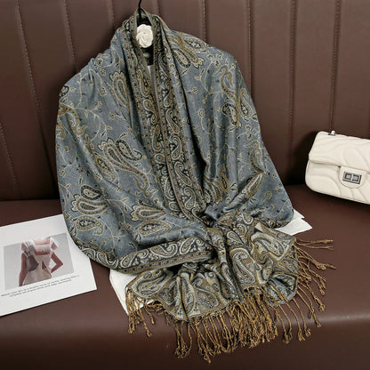 Gray paisley shawl with gold fringe on brown bench, next to white quilted handbag