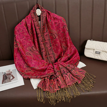 Red paisley pashmina scarf with gold fringe draped on a brown sofa next to a white purse