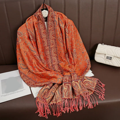 Orange paisley pashmina shawl with fringe on brown sofa, white purse beside