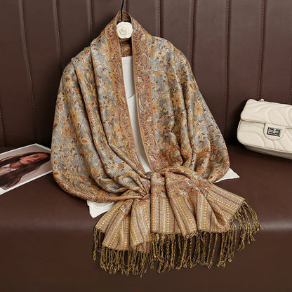 Paisley patterned shawl with fringe on brown couch, next to a beige quilted purse.