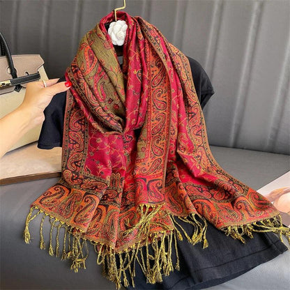 Red paisley pashmina scarf with gold fringe displayed on a hanger over black fabric