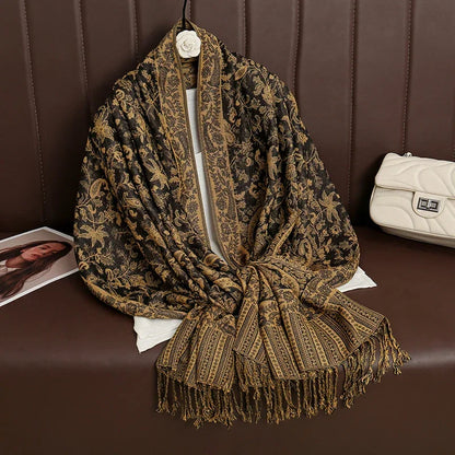 Black and gold floral paisley jacquard scarf with fringes on brown sofa, white purse nearby