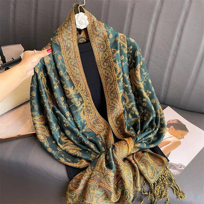 Green and gold paisley shawl with tassels draped on a hanger, displayed on a sofa