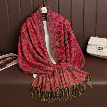 Pink paisley patterned shawl with gold tassels draped over a brown sofa, white purse nearby