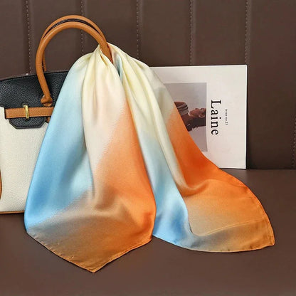 Gradient silk scarf with blue, orange, and cream draped on beige handbag, magazine nearby