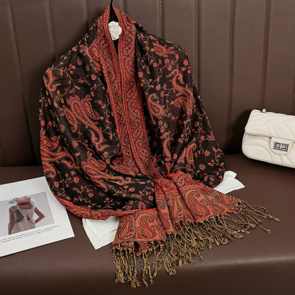 Paisley print black and red shawl with fringes displayed on a brown leather sofa