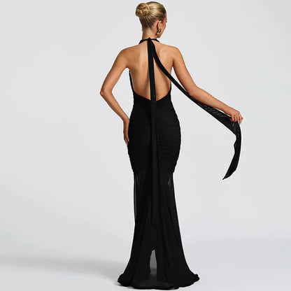 Woman in elegant black low-back gown with long flowing neck tie, posing against white background
