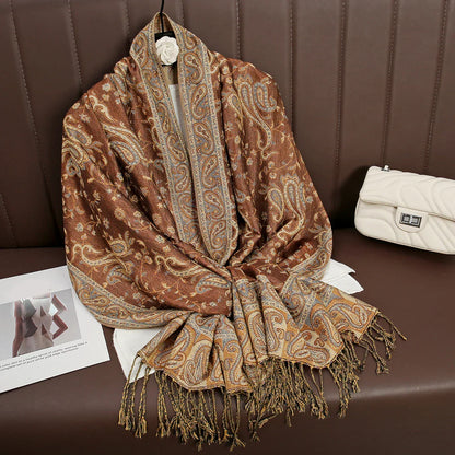 Brown paisley patterned shawl with fringe on brown sofa, next to white quilted handbag