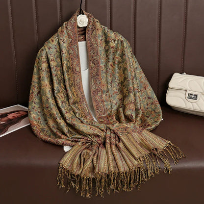 Floral paisley pashmina shawl with tassels on brown sofa, next to cream quilted handbag